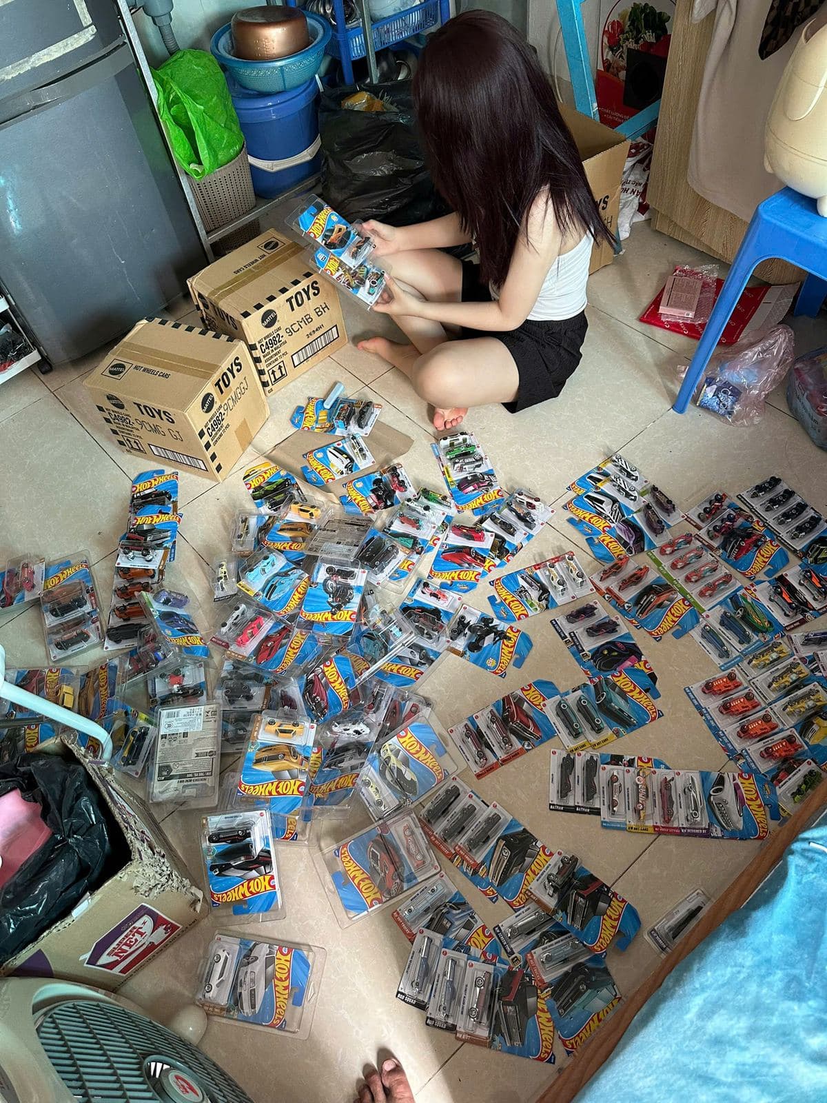 Phân loại hàng trăm vỉ Hot Wheels trải trên sàn, cạnh các thùng hàng vừa mở