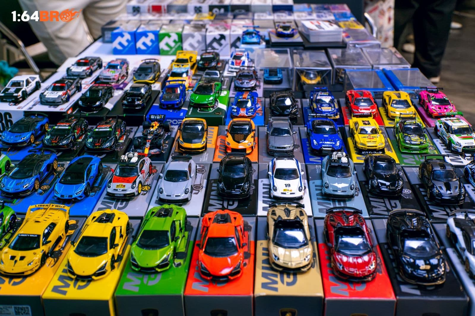 Hàng mô hình Mini GT 1:64 nhiều màu xếp trên hộp, gồm Lamborghini, Porsche 911 và Nissan GT-R