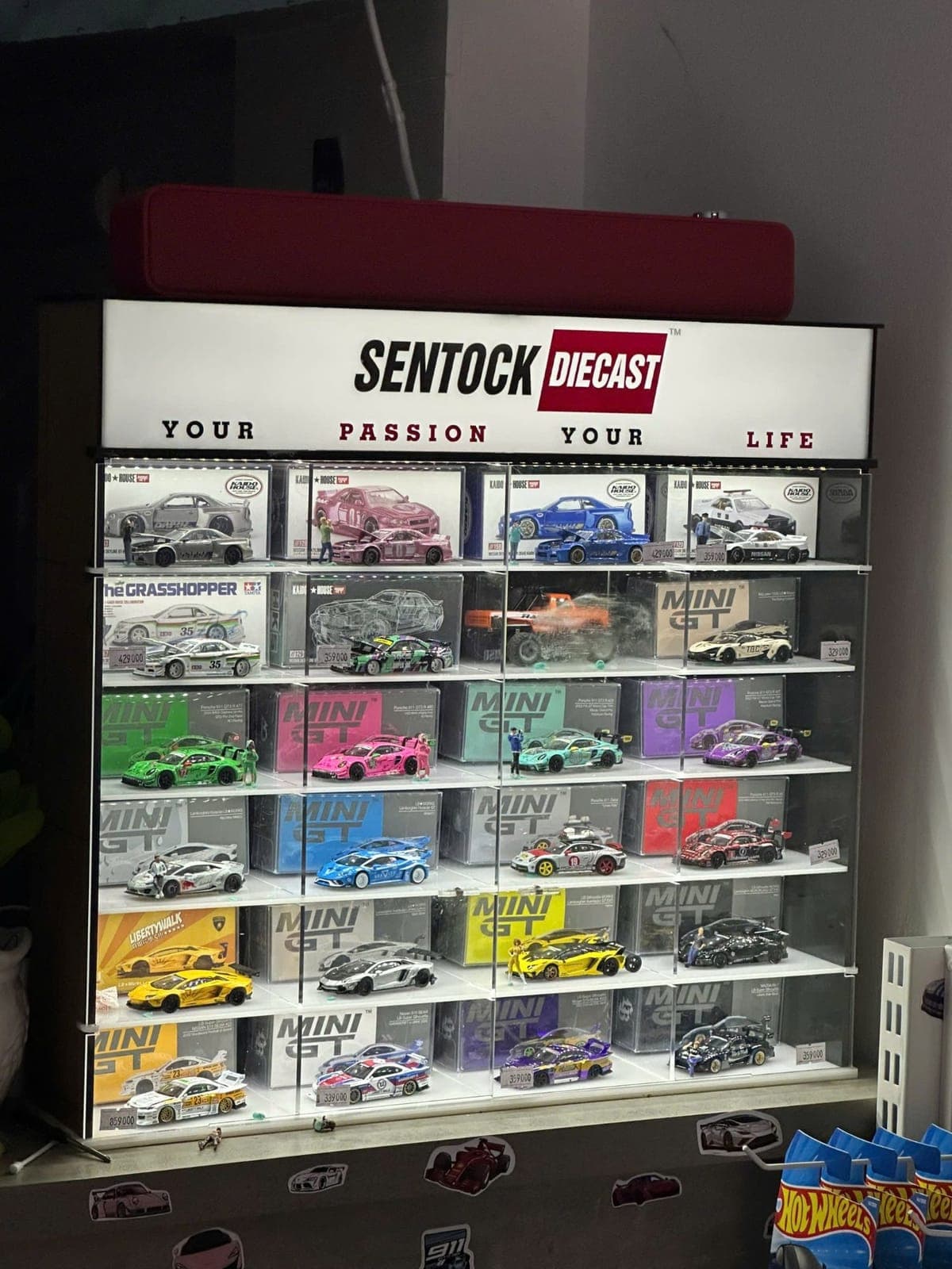 Tủ trưng bày tại cửa hàng Sentock Diecast: biển đèn "Sentock Diecast — Your passion, your life" và các hộp Kaido House, Mini GT tỉ lệ 1:64
