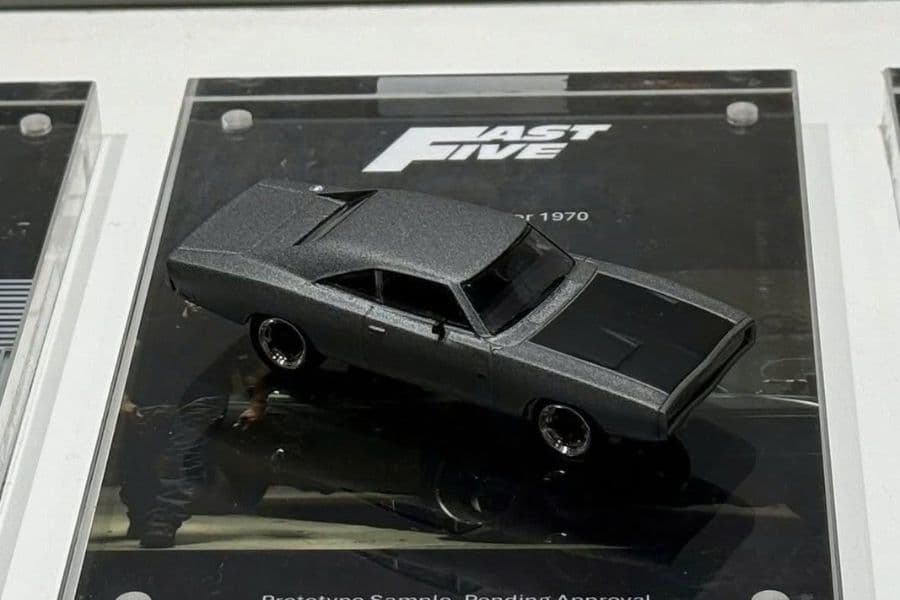 Mini GT MGT01256 Dodge Charger xám nắp capo sẫm màu, đặt trên tấm đế mica in logo FAST FIVE, chụp từ trên cao